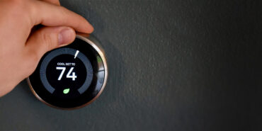 Hand adjusting temperature on smart thermostat to save energy and money. Green tech!